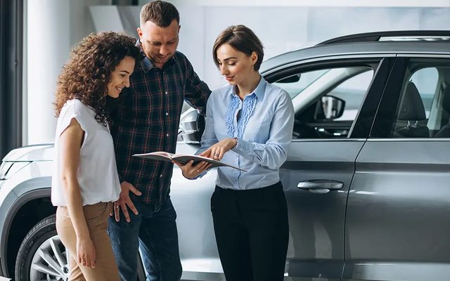 A couple going through paperwork with a saleswoman beside a car